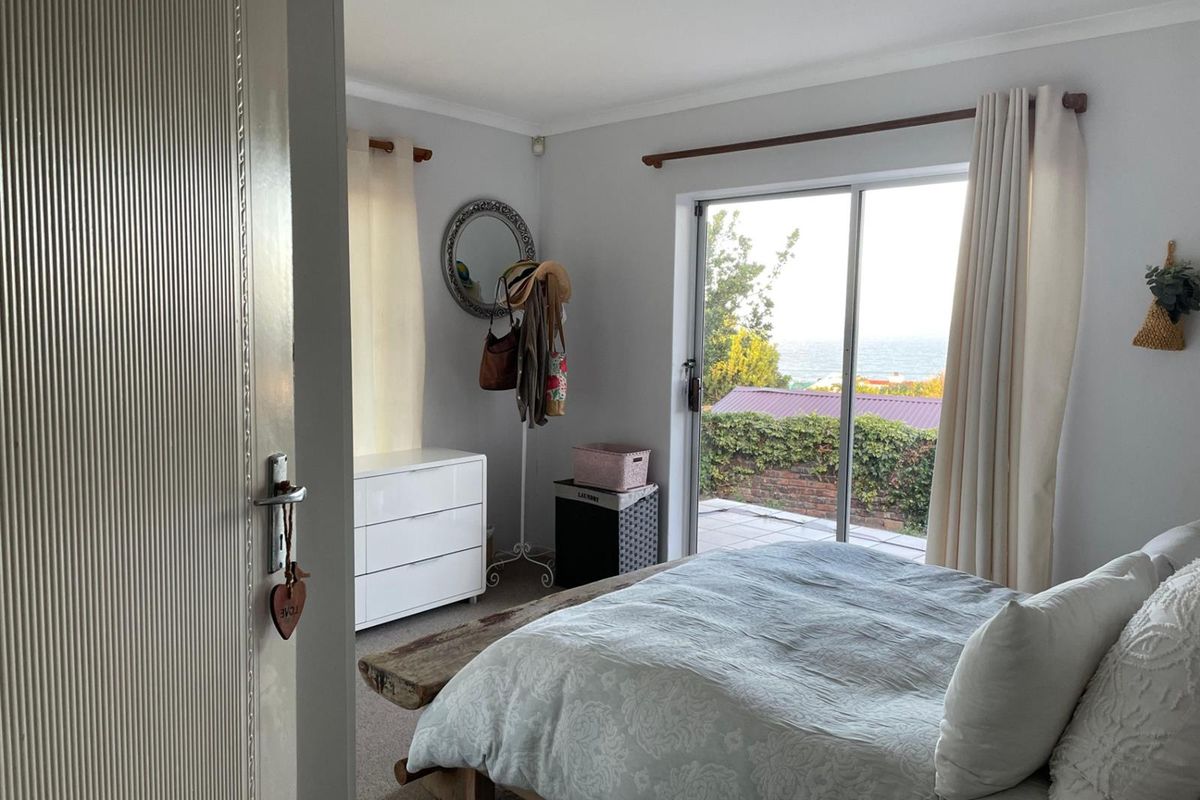 A bright bedroom featuring sliding glass doors that open to an outdoor patio area with coastal views.
