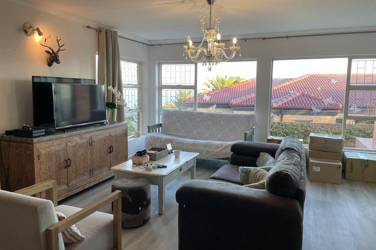 A bright living room featuring large windows, laminate flooring, and a decorative chandelier, offering a comfortable space for relaxation.