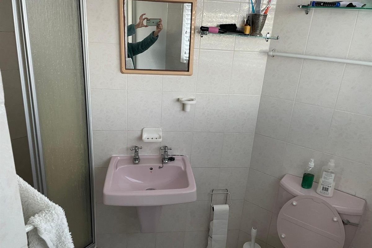 A compact bathroom featuring a vintage pink pedestal sink and matching toilet, complemented by white wall tiles and a glass shower enclosure.