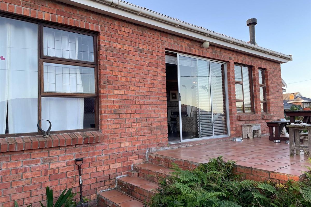 Rear exterior view of the house featuring a red brick facade, tiled patio area, and sliding glass doors providing access to the interior.