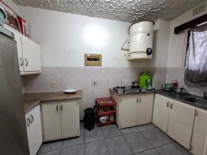 A functional kitchen featuring built-in cabinetry, tiled backsplash, and tiled flooring, equipped with a wall-mounted geyser and standard countertop workspace.