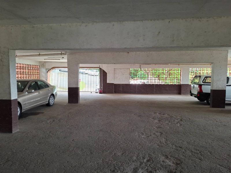A covered parking garage area featuring concrete flooring, structural pillars, and decorative breeze block ventilation panels.