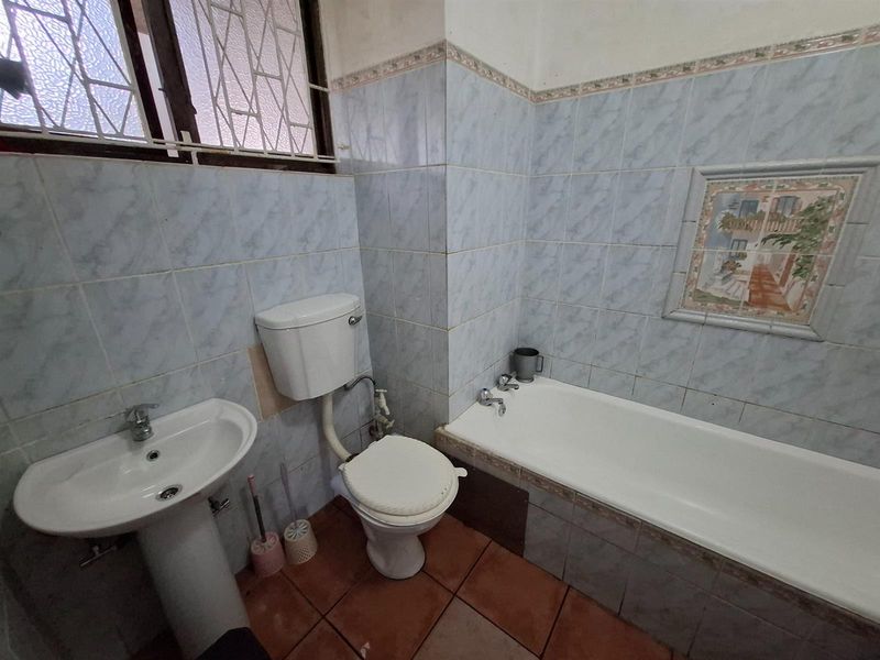 A dated bathroom featuring a pedestal basin, toilet, and bathtub with blue wall tiles and terracotta flooring, requiring cosmetic updates.