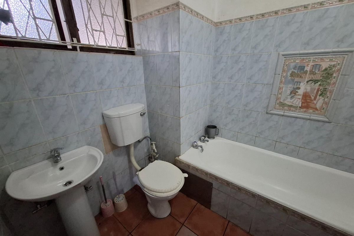 A dated bathroom featuring a pedestal basin, toilet, and bathtub with blue wall tiles and terracotta flooring, requiring cosmetic updates.