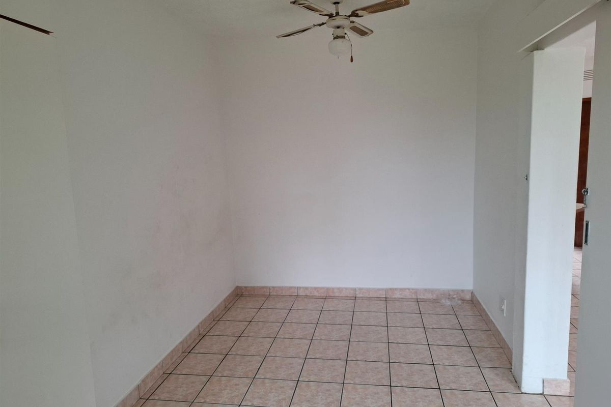 An empty, neutrally painted room featuring tiled flooring and a ceiling fan, offering a blank canvas for potential interior design updates.