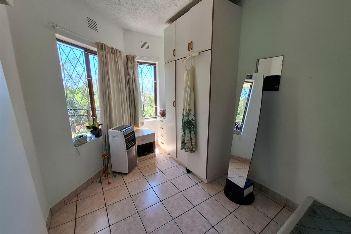 A bedroom featuring built-in cabinetry, tiled flooring, and large windows with security bars, offering a functional and well-lit living space.