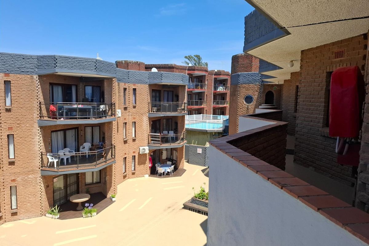 View of the apartment complex courtyard featuring brick facade architecture, multiple private balconies, and a communal pool area in the background.