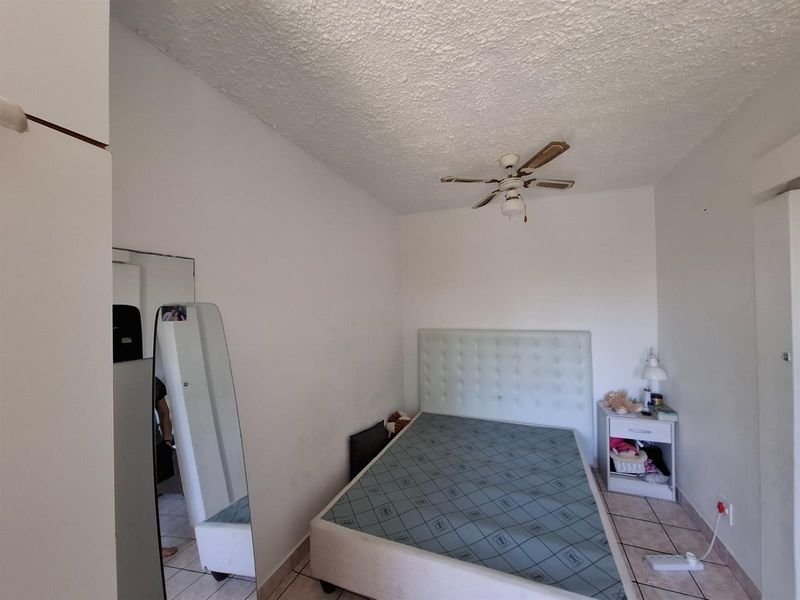 A functional bedroom featuring tiled flooring, a ceiling fan, and built-in storage, offering a neutral canvas for personalization.