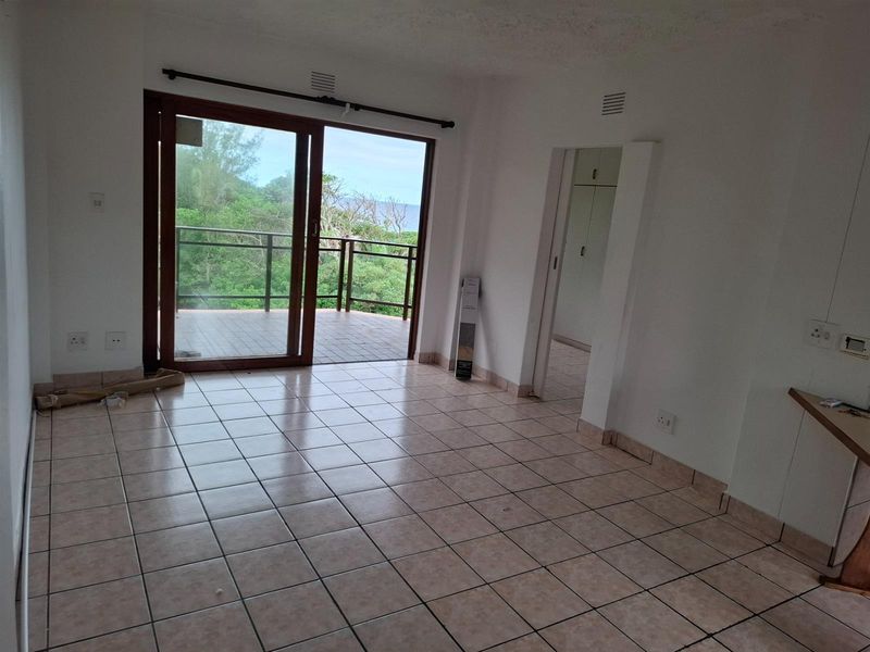 An open-plan living area featuring ceramic floor tiles, sliding glass doors leading to a balcony, and access to an adjacent room.