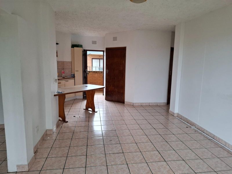 An open-plan living and kitchen area featuring tiled flooring, neutral walls, and direct access to an outdoor balcony space.