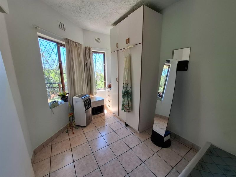 A bedroom featuring built-in cabinetry, tiled flooring, and large windows with security bars, offering a functional and well-lit living space.