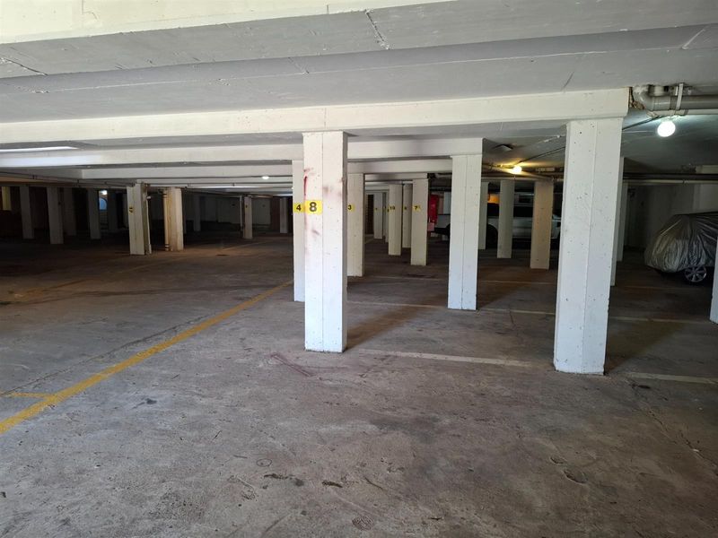 A spacious, covered basement parking area featuring concrete structural columns and marked parking bays within an apartment complex.