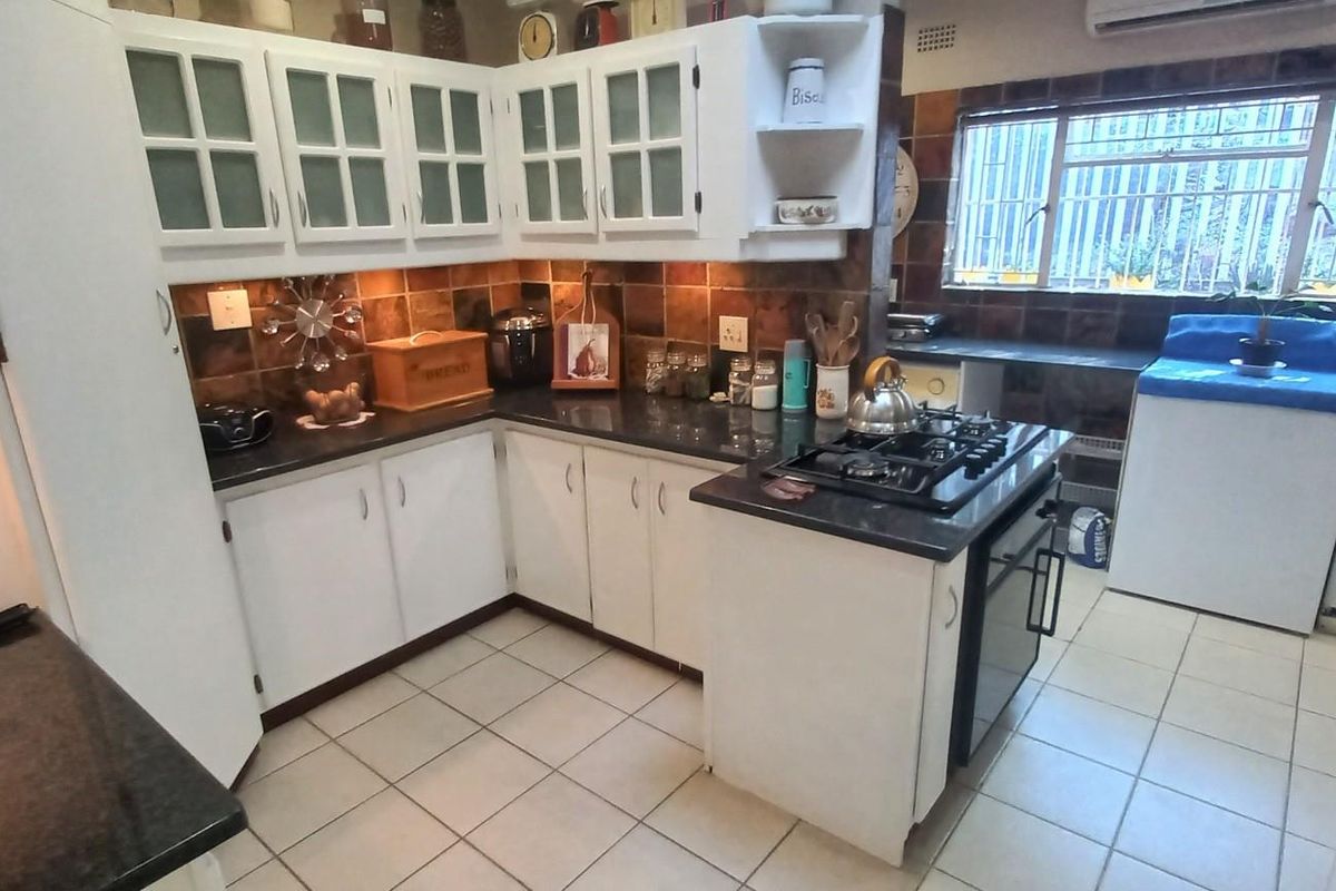 A functional kitchen featuring white cabinetry, dark granite countertops, a gas hob, and tiled backsplash, offering a classic layout with ample storage space.