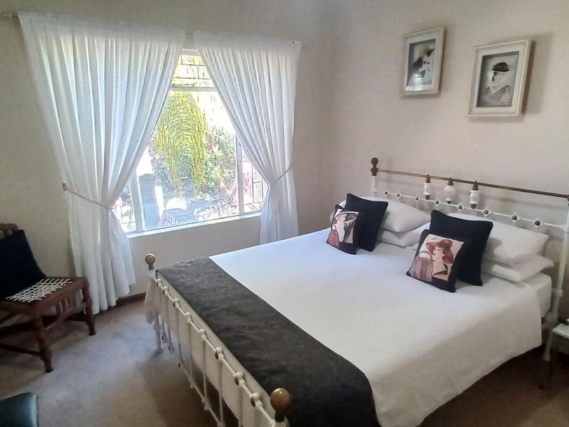 A standard bedroom featuring neutral wall tones, carpeted flooring, and a window with curtains allowing natural light.