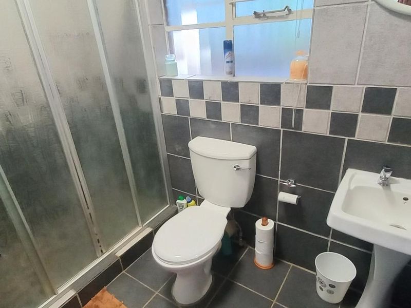 A functional bathroom featuring a shower enclosure, pedestal basin, and toilet with tiled walls and flooring.