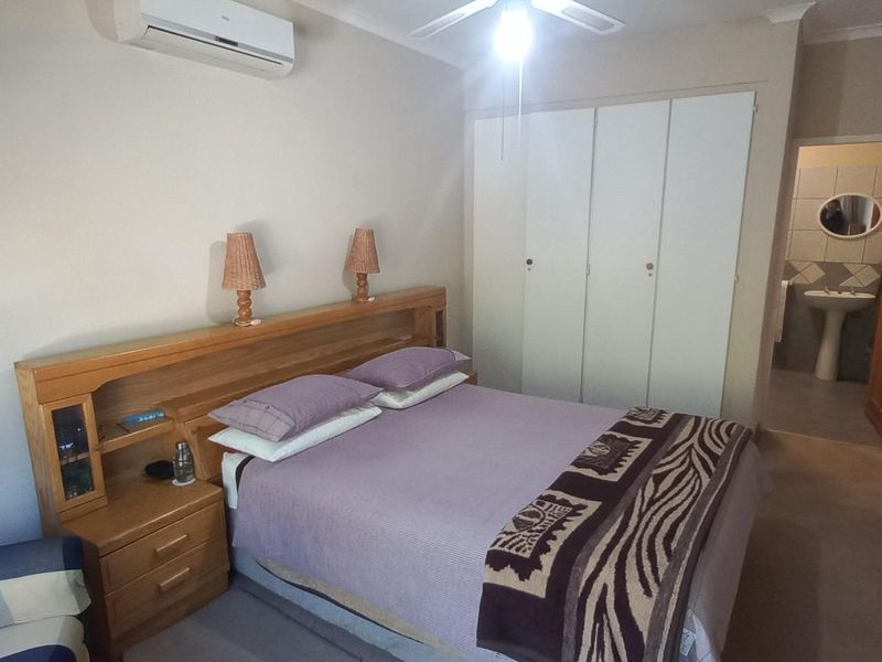 A functional bedroom featuring built-in cupboards, a ceiling fan, and a wall-mounted air conditioning unit, with direct access to an en-suite bathroom.