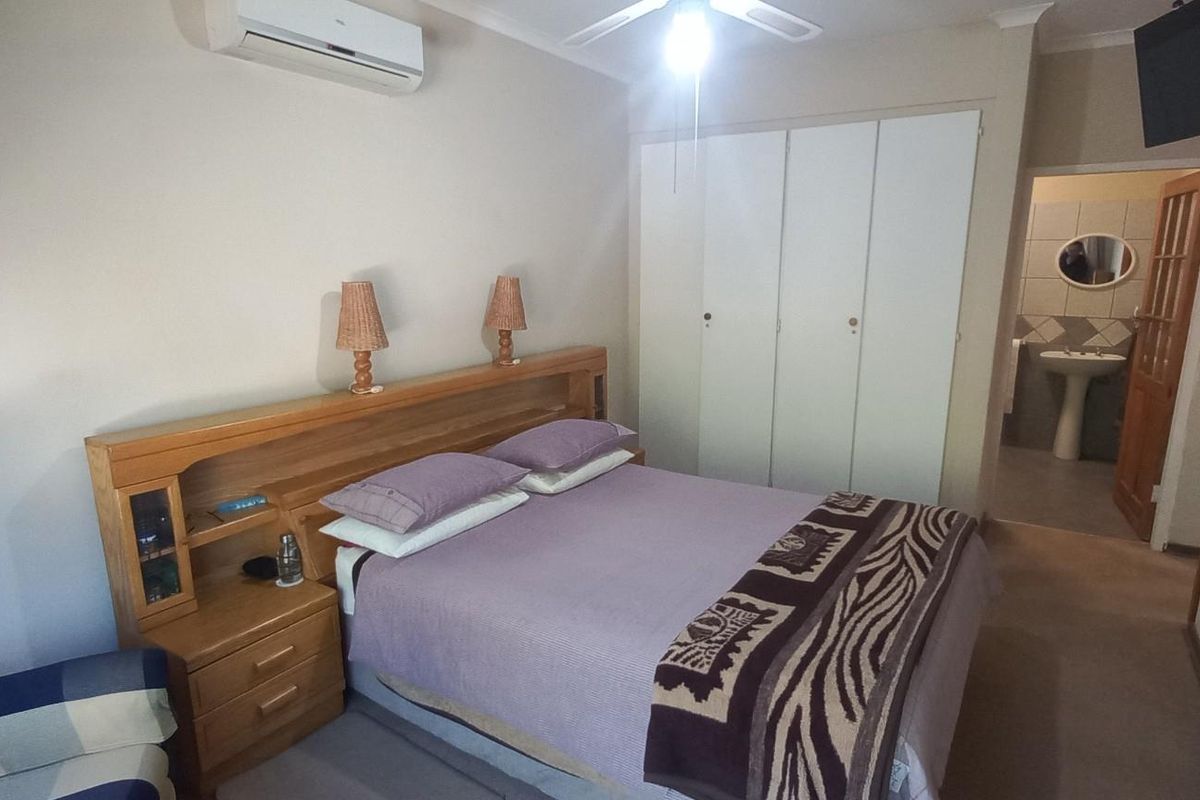 A functional bedroom featuring built-in cupboards, a ceiling fan, and a wall-mounted air conditioning unit, with direct access to an en-suite bathroom.