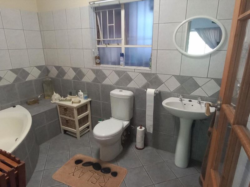 A functional bathroom featuring a built-in bathtub, pedestal basin, toilet, and neutral wall and floor tiling with a decorative border.