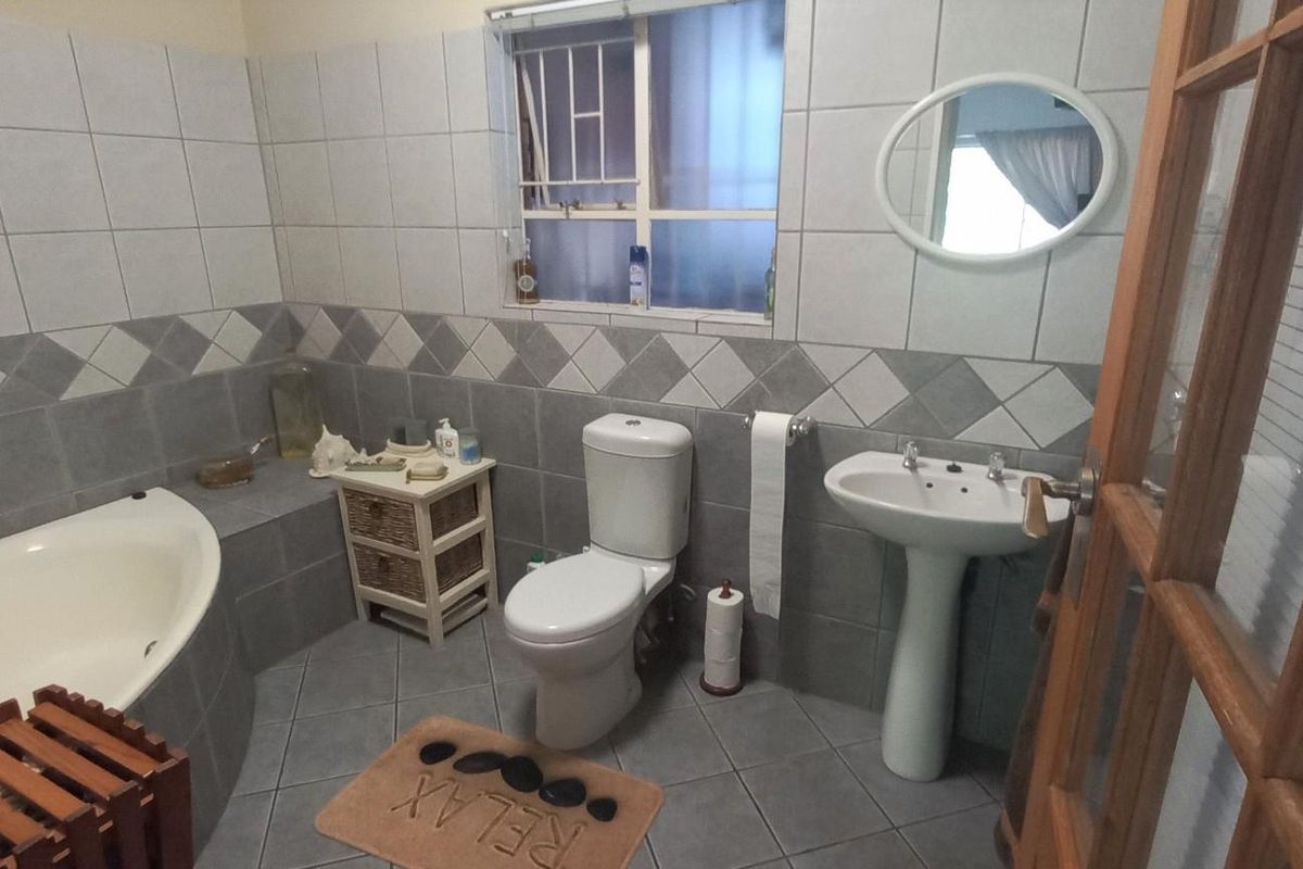 A functional bathroom featuring a built-in bathtub, pedestal basin, toilet, and neutral wall and floor tiling with a decorative border.