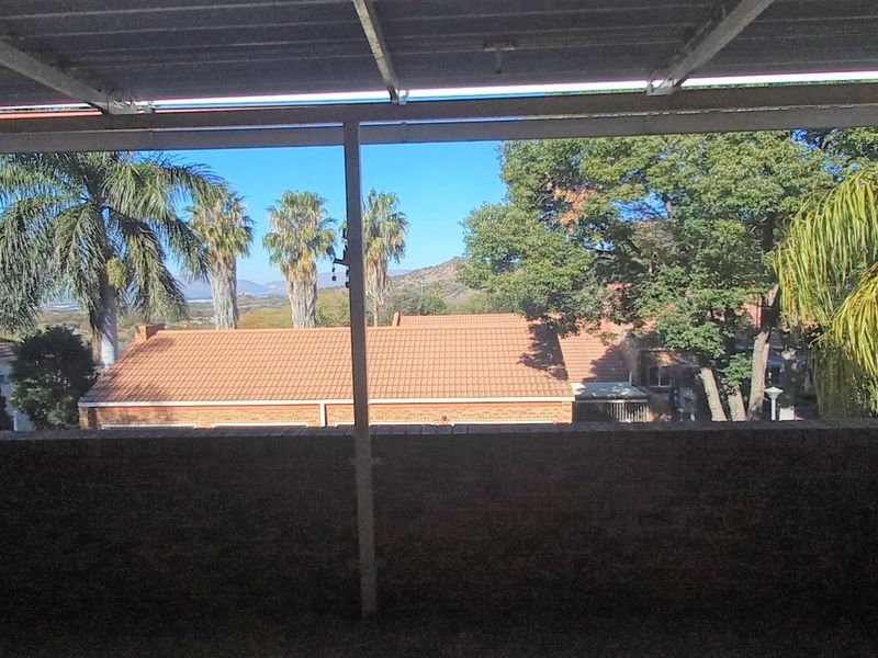 A covered outdoor patio featuring a brick balustrade and metal roofing, offering elevated views of the surrounding neighborhood and landscape.