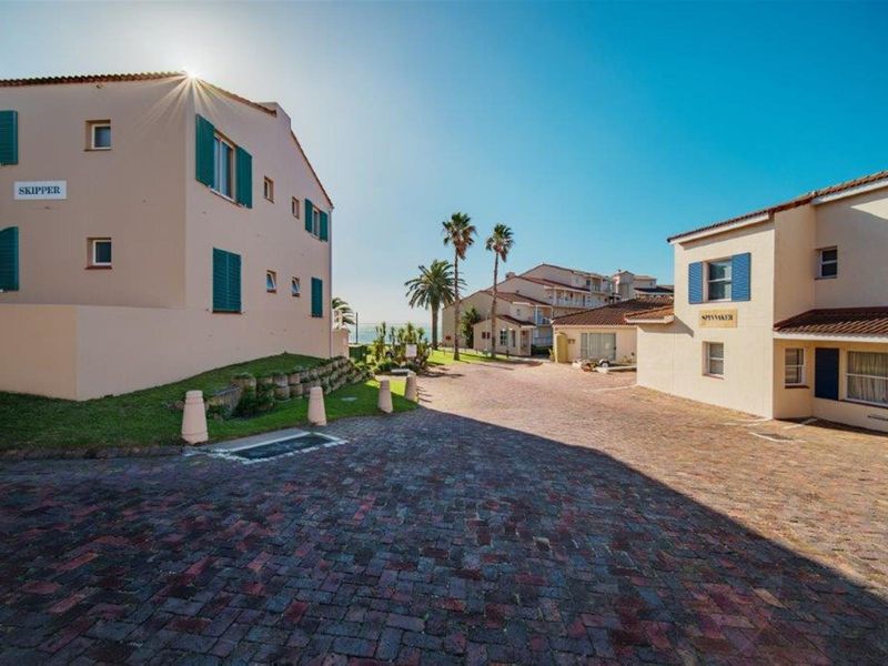 Exterior view of the apartment complex entrance featuring paved driveway, landscaped garden areas, and traditional building architecture with shutters.