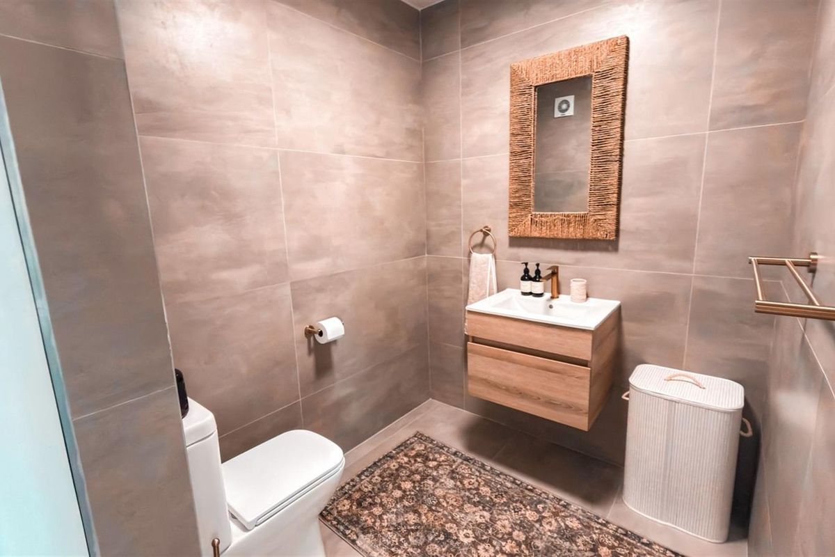 Modern bathroom featuring large format wall tiles, a wall-mounted timber vanity with a brass faucet, and contemporary fixtures.