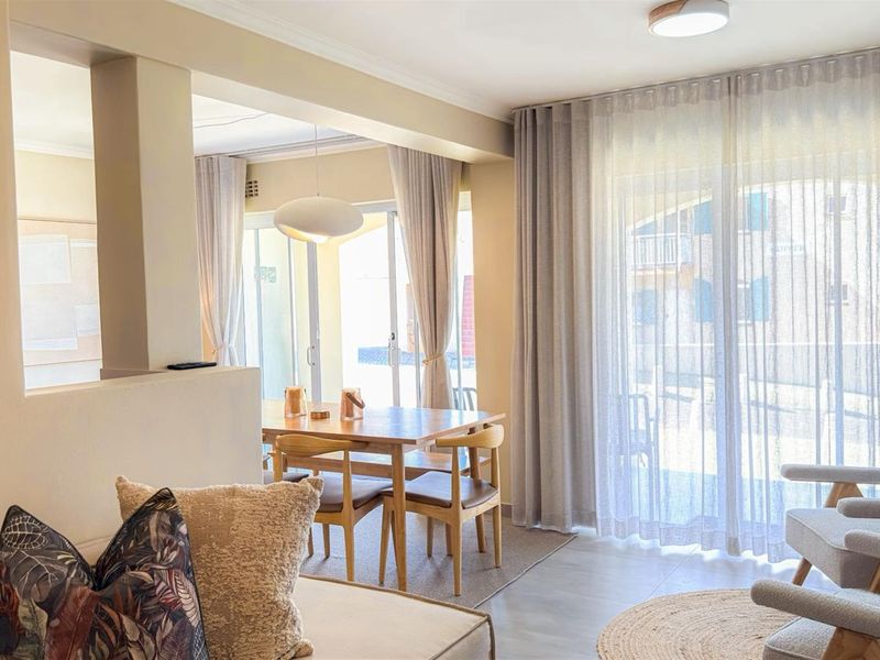 Bright open-plan living and dining area featuring tiled flooring, neutral walls, and large sliding glass doors providing access to the outdoor space.