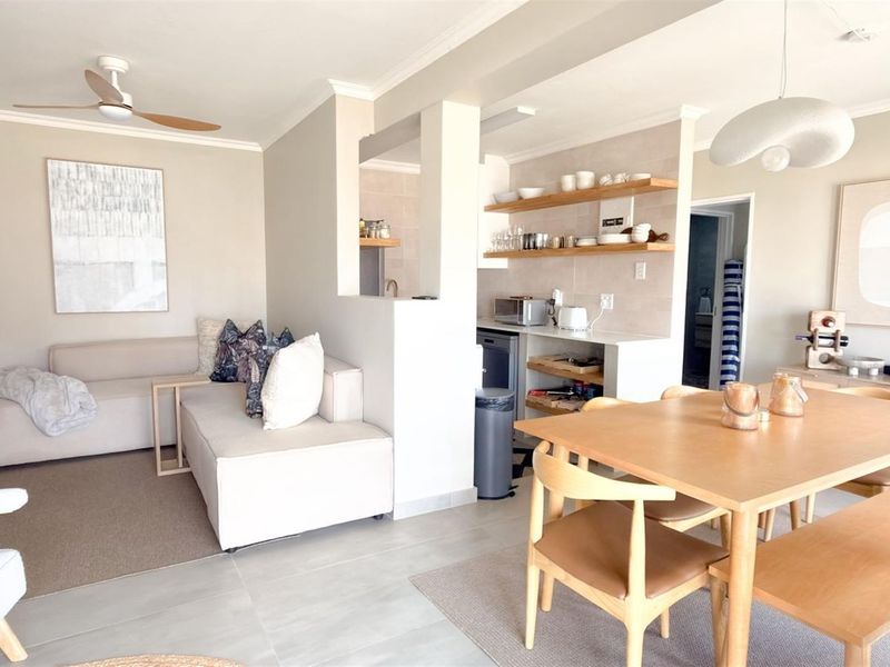 A bright and modern open-plan living and dining area featuring neutral tones, tiled flooring, and integrated shelving in the kitchen nook.