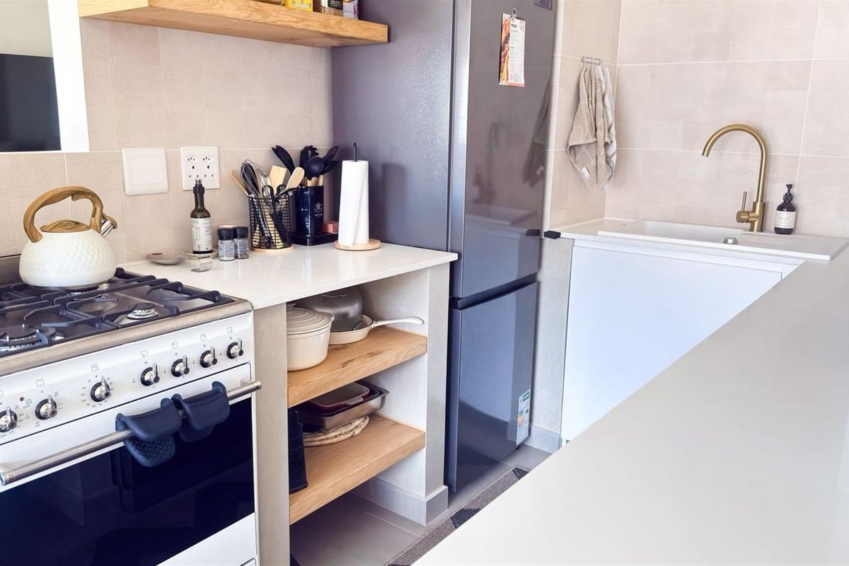 Modern kitchen featuring a gas stove, quartz countertops, open timber shelving, and a stylish brass faucet with an undermount sink.