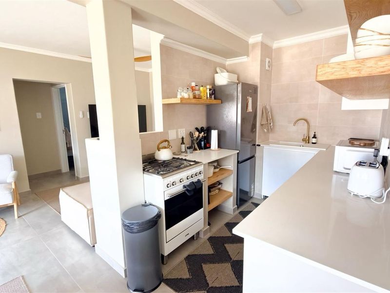 Modern open-plan kitchen featuring stone countertops, brass fixtures, gas stove, and floating timber shelving, seamlessly integrated with the adjacent living area.