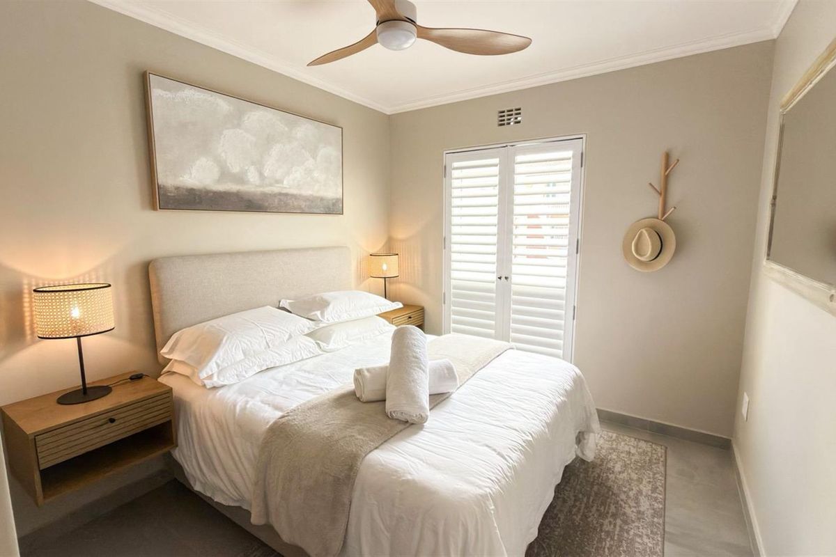 A well-maintained bedroom featuring neutral tones, tiled flooring, a ceiling fan, and plantation shutters providing natural light control.