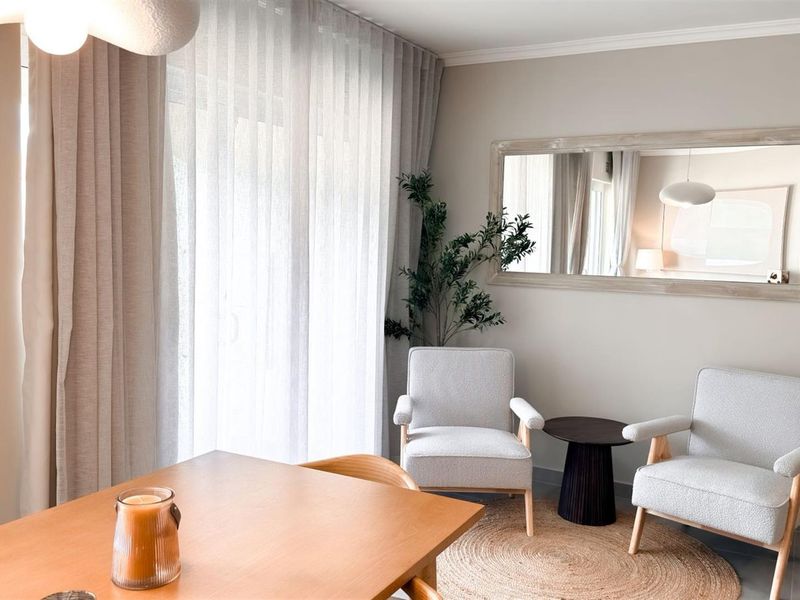 A bright and well-maintained living area featuring neutral wall tones, tiled flooring, and large windows with floor-to-ceiling curtains.