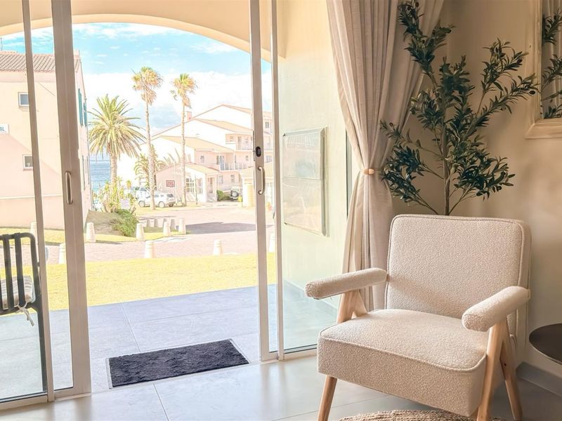 A bright living area featuring large sliding glass doors that open onto a patio with views of the surrounding coastal complex.
