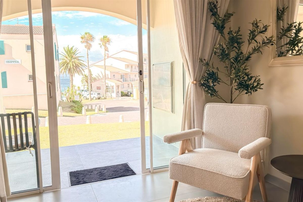 A bright living area featuring large sliding glass doors that open onto a patio with views of the surrounding coastal complex.