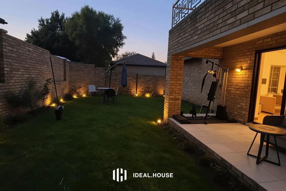 A well-maintained rear garden featuring a paved patio area, brick boundary walls, and integrated outdoor lighting, perfect for evening relaxation.