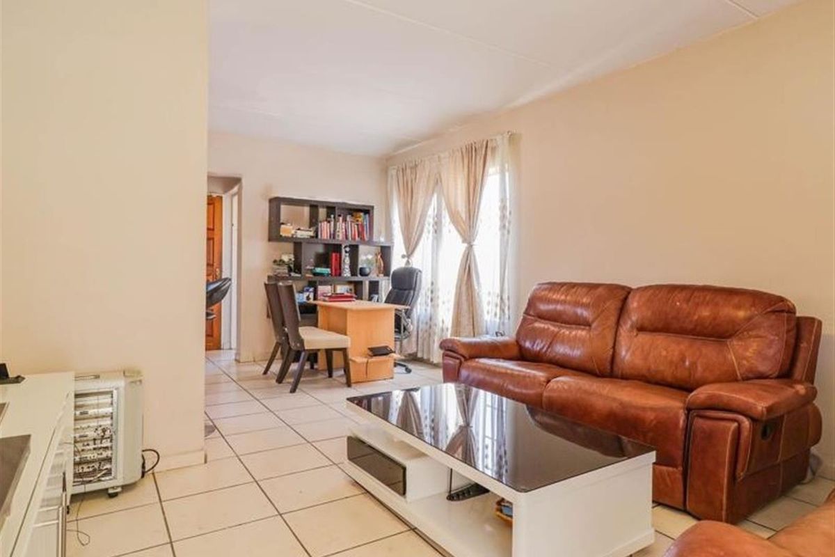 A living room area featuring tiled flooring and a neutral wall finish, providing a functional space for relaxation and home office use.