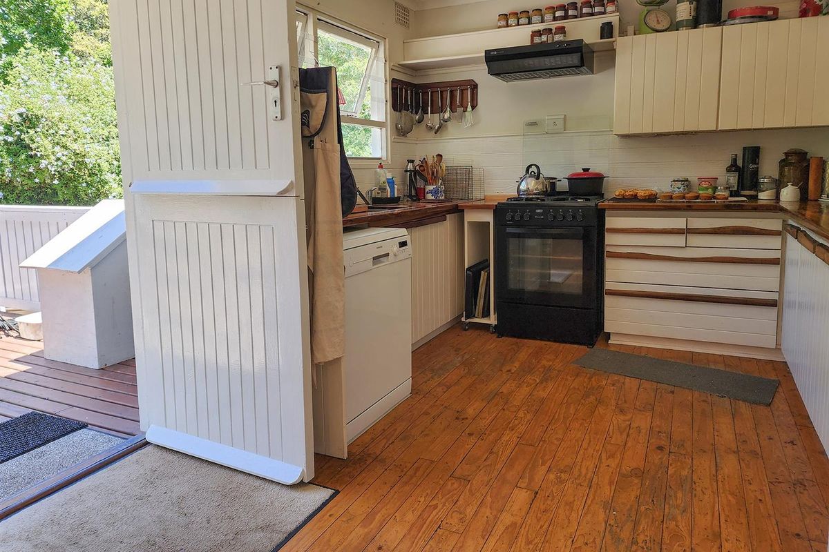 A functional kitchen featuring timber flooring, built-in cabinetry, a gas stove with extractor fan, and direct access to an outdoor deck area.