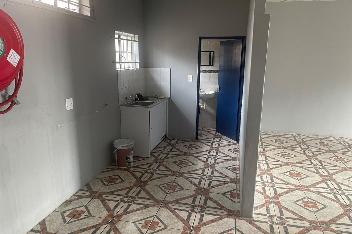 A functional kitchenette area with a single sink unit, tiled flooring, and an adjacent small bathroom, suitable for a compact retail or office space.