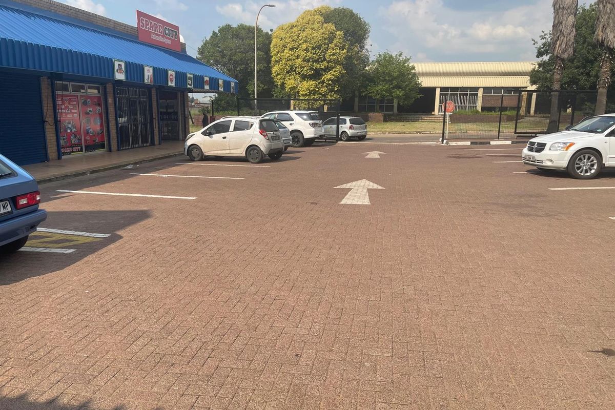 Exterior view of a retail property featuring a paved parking area with marked bays and a blue metal awning over the storefront entrance.