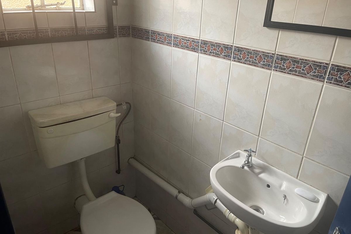 A compact bathroom featuring a standard toilet, wall-mounted basin, and full-height wall tiling with decorative border accents.