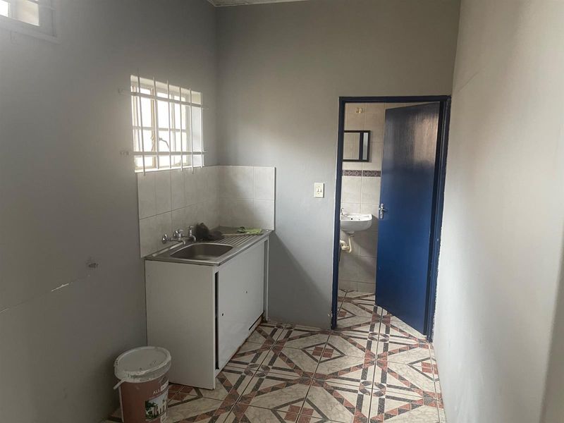 A functional utility space featuring a stainless steel sink unit, tiled splashback, and direct access to an adjoining bathroom.