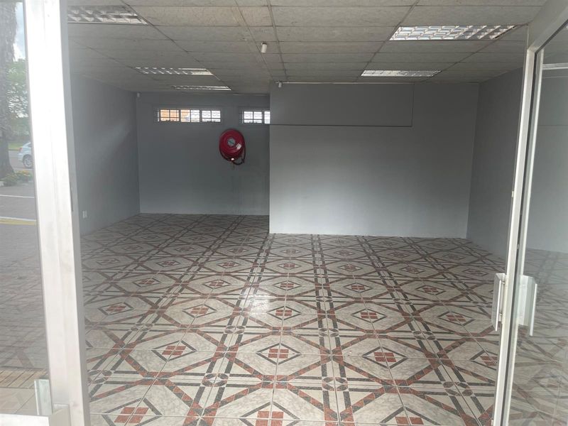 An empty retail space featuring patterned ceramic floor tiles, recessed ceiling lighting, and a wall-mounted fire hose reel.