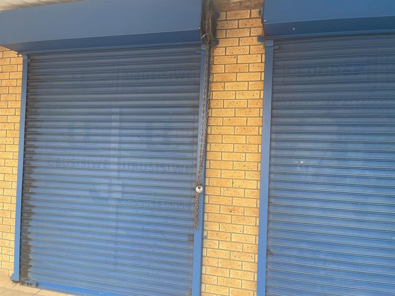 Retail storefront featuring blue metal roller shutter doors with manual chain operation and brick facade detailing.