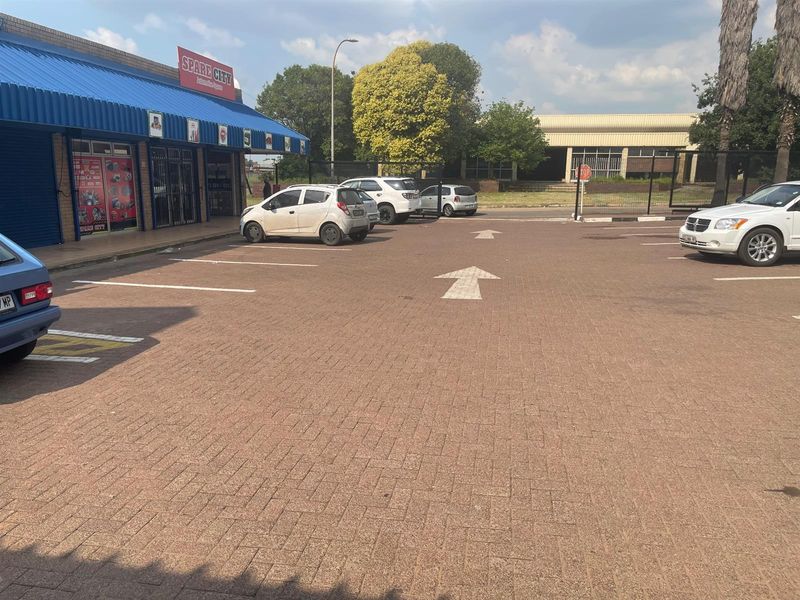 Exterior view of a retail property featuring a paved parking area with marked bays and a blue metal awning over the storefront entrance.