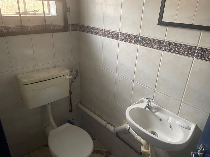 A compact bathroom featuring a standard toilet, wall-mounted basin, and full-height wall tiling with decorative border accents.