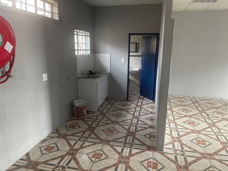 A functional kitchenette area with a single sink unit, tiled flooring, and an adjacent small bathroom, suitable for a compact retail or office space.