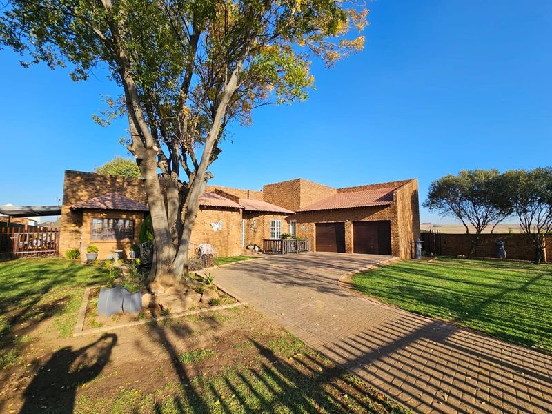 A well-maintained face-brick house featuring a paved driveway, double garage, and established garden with mature trees.