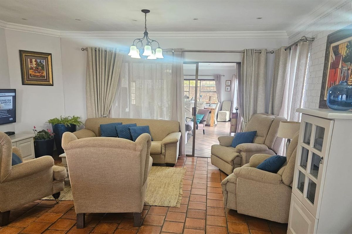 A comfortable living room featuring terracotta floor tiles, crown molding, and sliding glass doors that open onto an adjacent patio area.