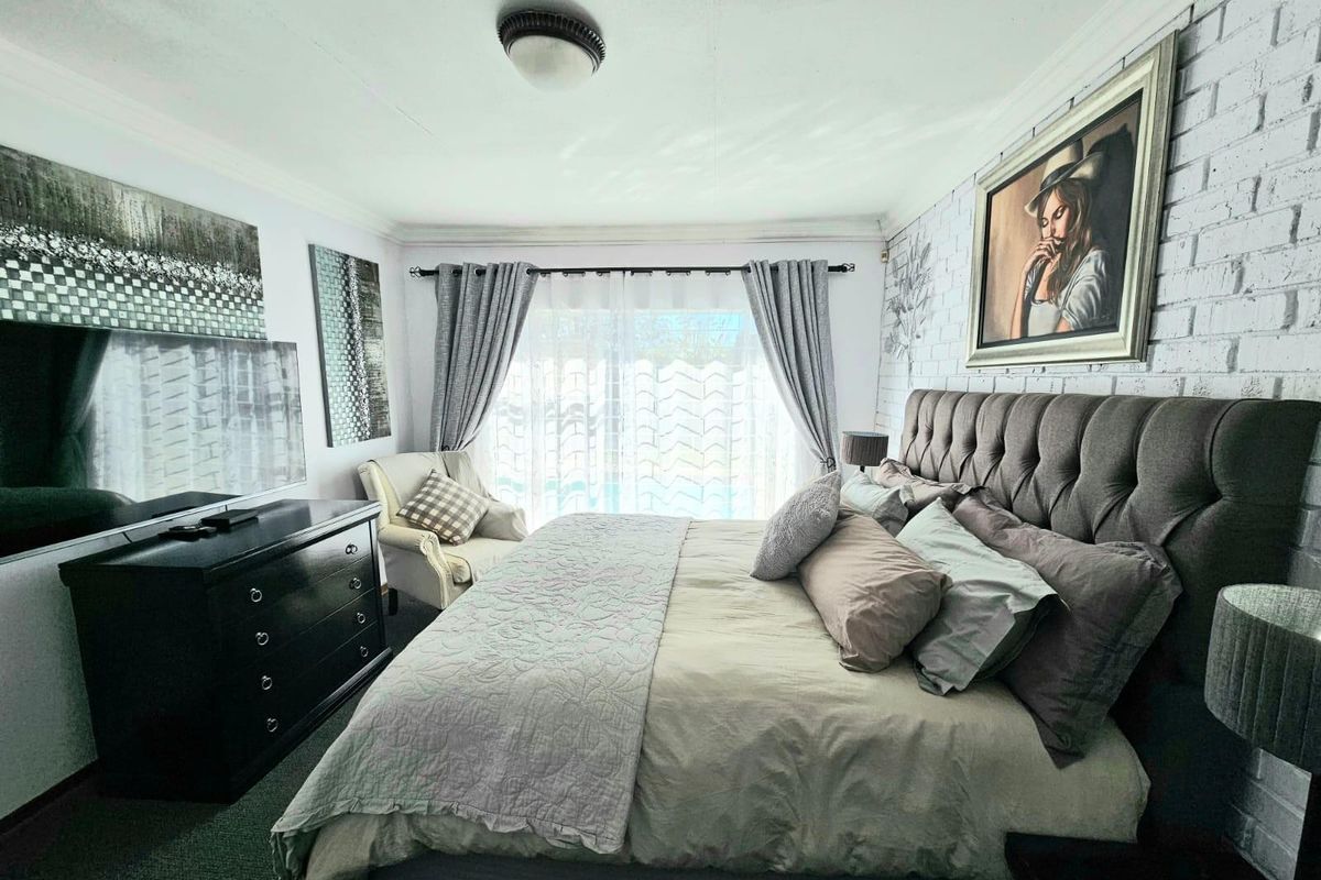 A well-maintained bedroom featuring a textured white brick accent wall, neutral carpeting, and large sliding glass doors providing natural light.