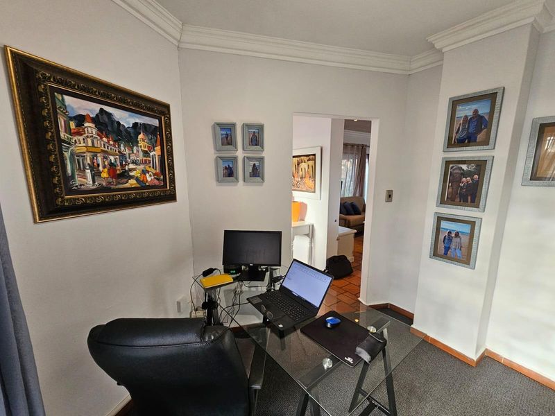 A functional home office space featuring carpeted flooring and crown molding, with a doorway leading to an adjacent living area.